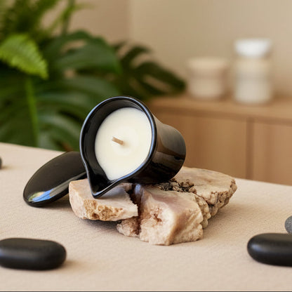 Black massage candle holder with a white candle on a rock surface